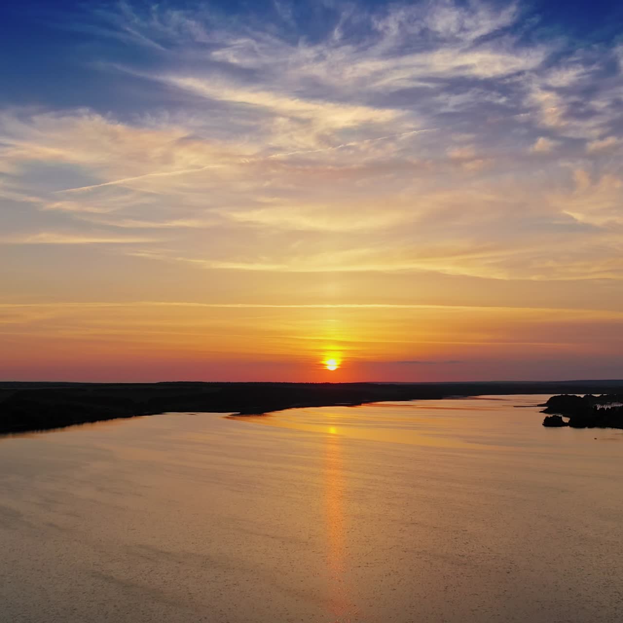 Golden path over the river at sunset. Beautiful view on the natural landscape with evening sun that reflects in water. Camera moves down.