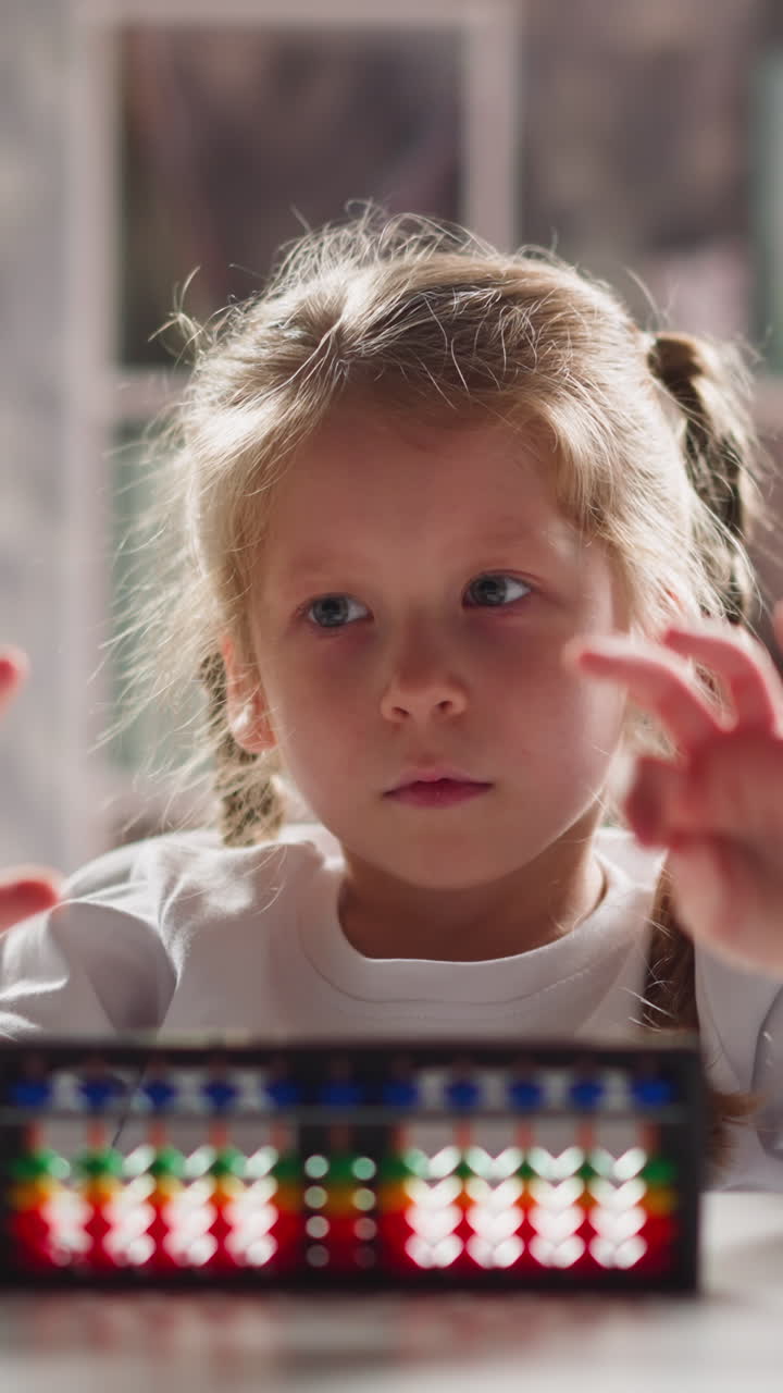 Cute little girl student with colorful abacus does exercises for fingers sitting at table during maths lesson in kindergarten close view slow motion