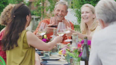 group of mature friends talking and making a toast with wine at summer party in garden at home