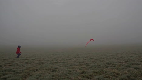 child flying kite in foggy field