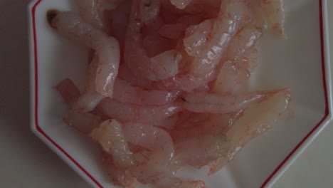 Raw-peeled-shrimp-or-prawns-on-small-white-plate,-Overhead-Slide-Down