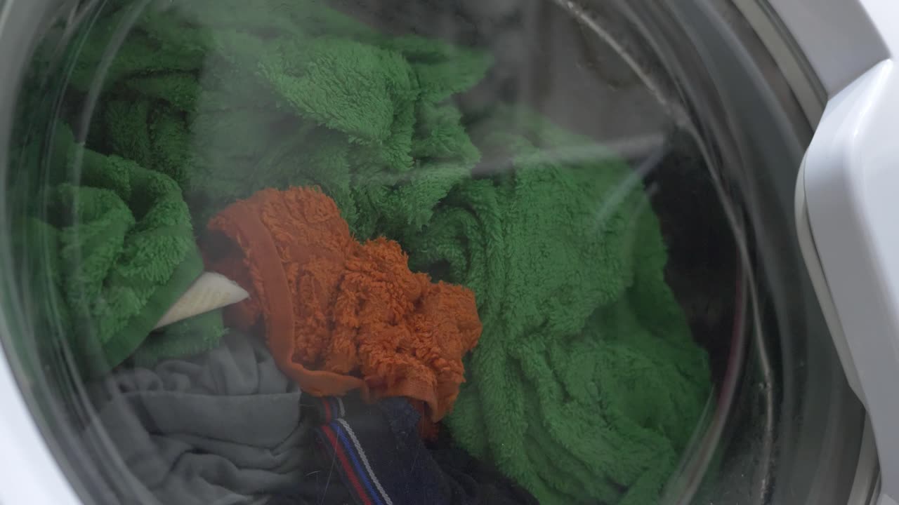 A washing machine is filled with a large pile of laundry. Overflowing with garments