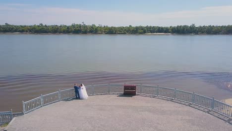 newlywed couple looks at river from viewpoint aerial view