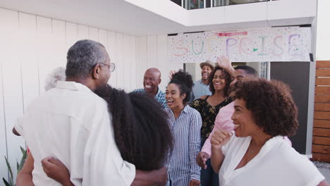 Black-family-running-to-welcome-grandparents-outside-their-home-for-a-surprise-party,-back-view