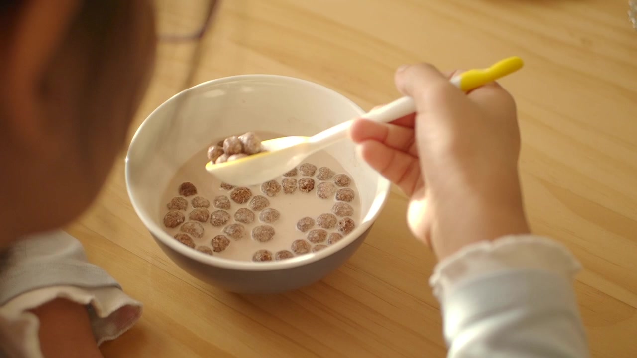 Bambino che Mangia Cereali al Cioccolato con Latte da una Ciotola