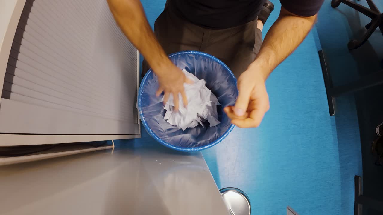 Overhead shot of a stressed person urgently digging through an office trash bin to find a missing sheet with critical information. Strong for concepts like data loss, document disposal mistakes, priva