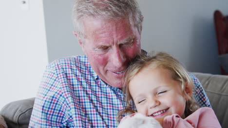 loving grandfather cuddling granddaughter holding soft toy rabbit at home