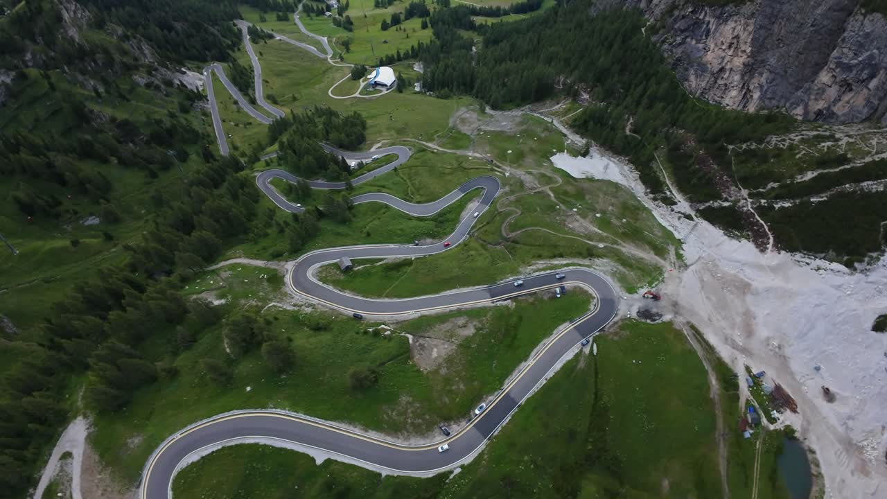 Aerial View Serpentine Switchbacks Dolomites, Dramatic Hairpin Turns Carve Through Steep Alpine Slopes And Gravel Terraces, Lone Vehicles Navigate Tight Curvature Under Towering Cliffs, Cinematic