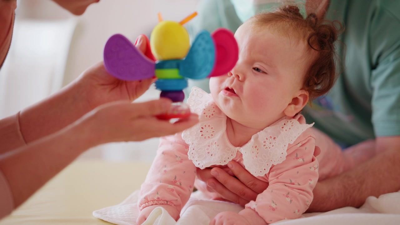 Baby lying on the stomach and focusing on a colorful toy held by an adult during a developmental activity