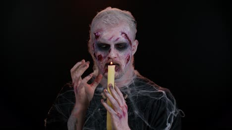 Zombie-man-with-makeup-with-fake-wounds-scars-and-white-contact-lenses-spells-conjures-over-a-candle