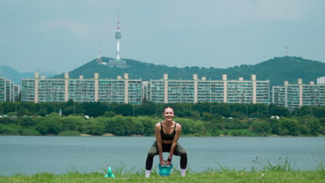 Fitness-Frau-Trainiert-Im-Freien-Und-Macht-Kettlebell-Schaukeln-Am-Flussufer-Mit-Dem-Malerischen-Seoul-Tower-Im-Hintergrund