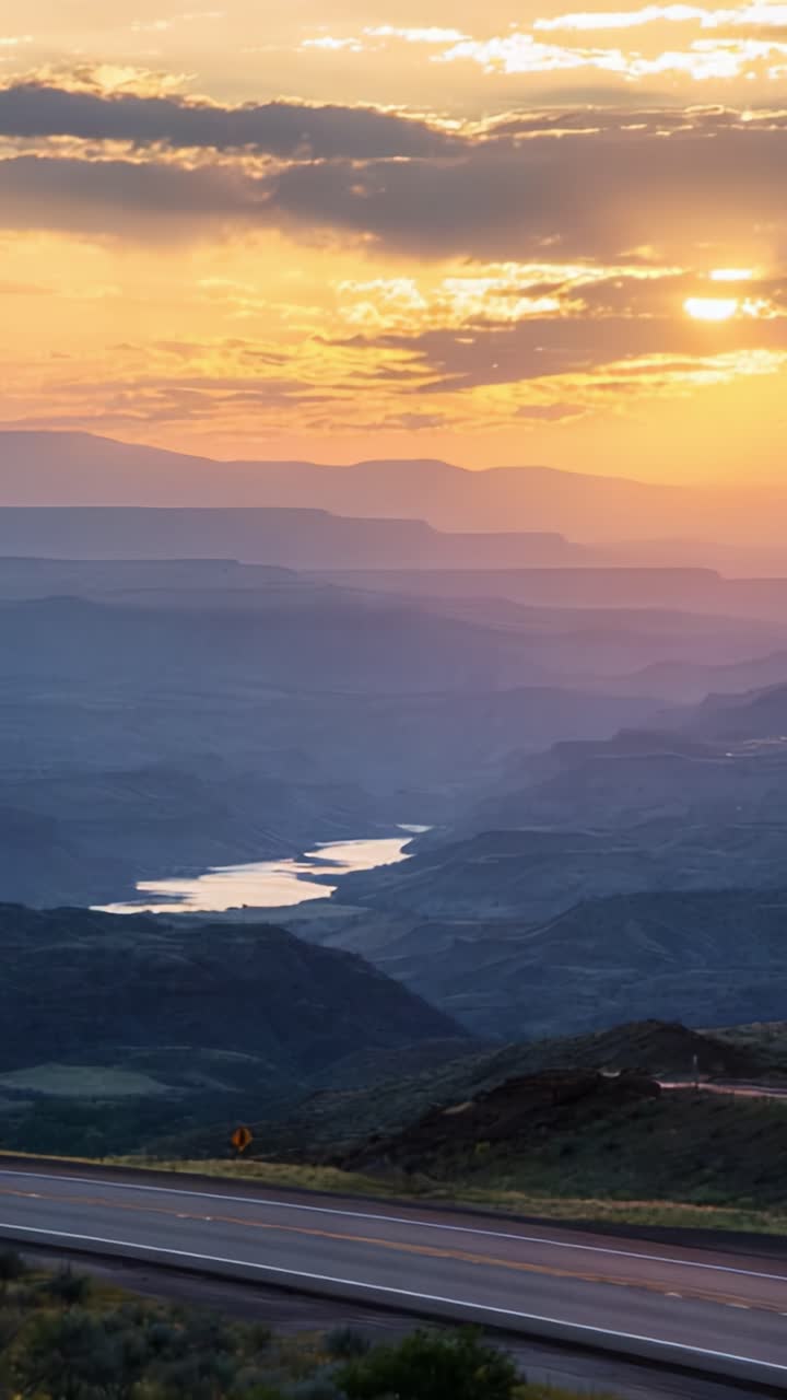 Fredfyldt solnedgang over et majestætisk canyonlandskab med en lastbil, der kører ad den snoede vej midt i livlige farver og lagdelte bjerge
