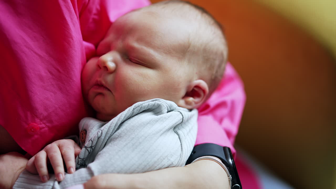 Lovely Caucasian baby sleeping in mom's arms. Caring mother sits and waves her newborn child. Close up.