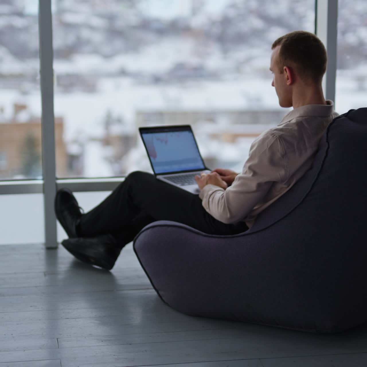 Working man sits with his back to the camera typing on his laptop. Male employee building charts on computer. City panorama in blur at backdrop