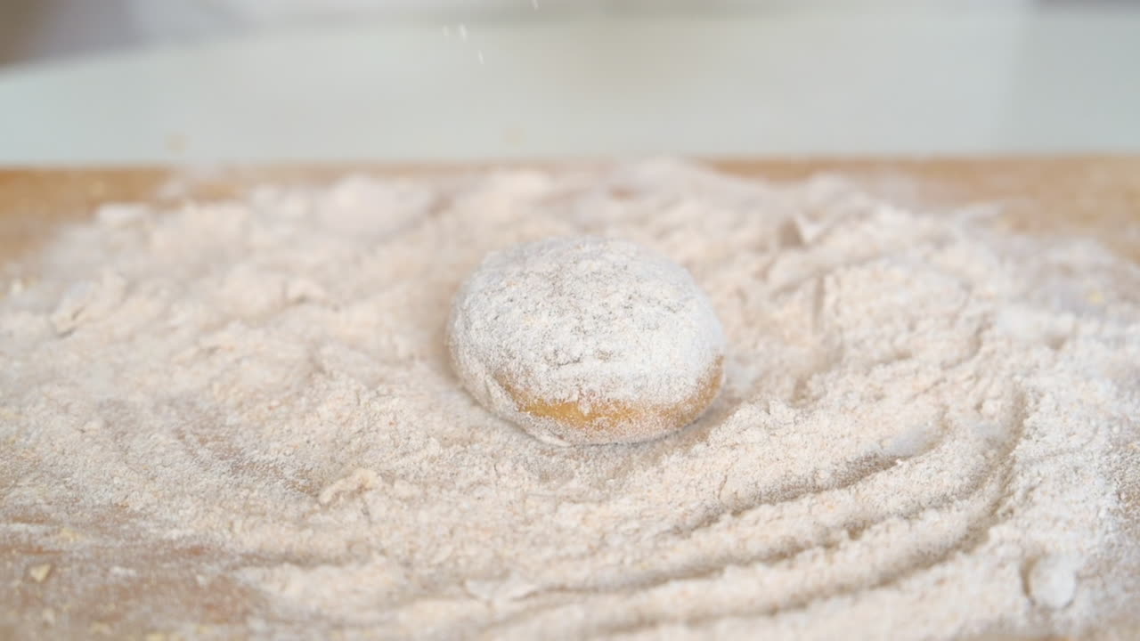 Woman wearing an apron, adding flour to dough on a wooden cutting board in the kitchen
