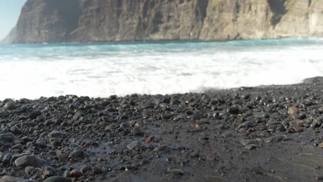 Tenerife-Beach-Close-Up-Volcanic-Sand-and-Pebbles-with-a-Reveal-Panning-Up-to-Ocean-Waves-and-Cliffs-at-Los-Gigantes,-Tenerife