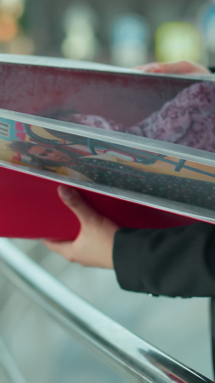 Vista lateral de uma mulher de blazer preto folheando seu livro de arte colorido, segurando uma pasta vermelha com trabalhos criativos, com fundo suavemente desfocado de um cenário urbano e corrimão de metal sob luz natural