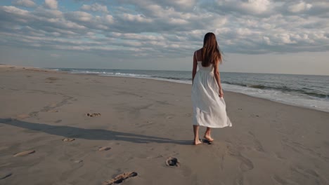 woman in white dress walking on the beach at sunset