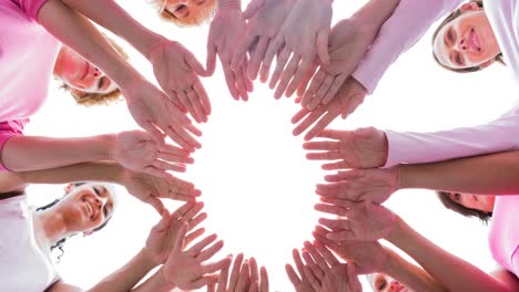 Diverse-group-of-smiling-women-touching-hands-outdoors-in-the-sun