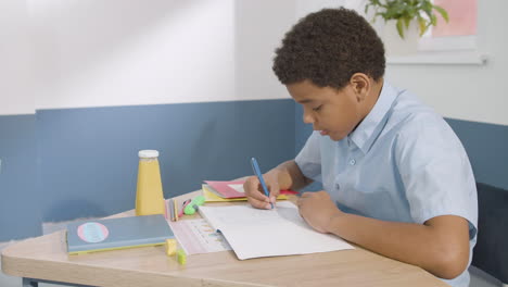 niño sentado en el escritorio y escribiendo en un cuaderno durante la clase de inglés en la escuela 1