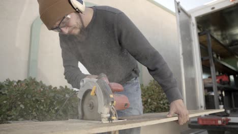 carpenter wearing ppe, ear muffs and safety glasses, cuts wood with circular saw