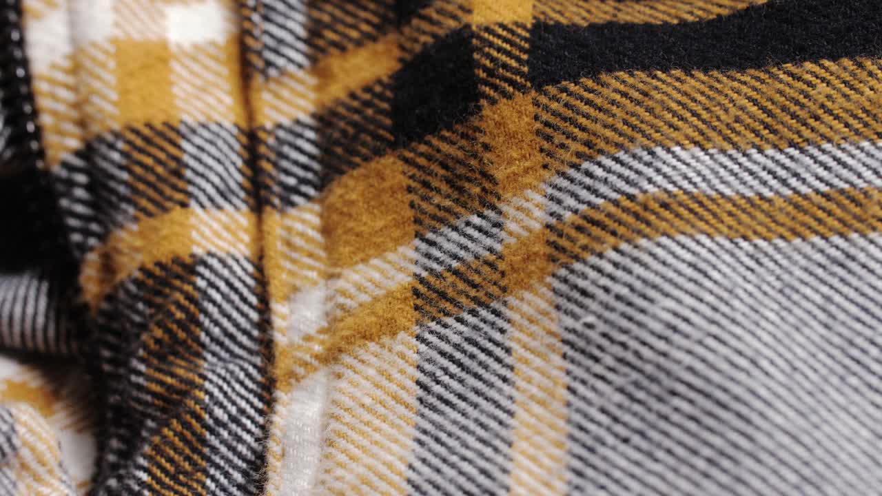 A mustard, black and white plaid flannel jacket reveals zipper and stitch details during a slow macro pan