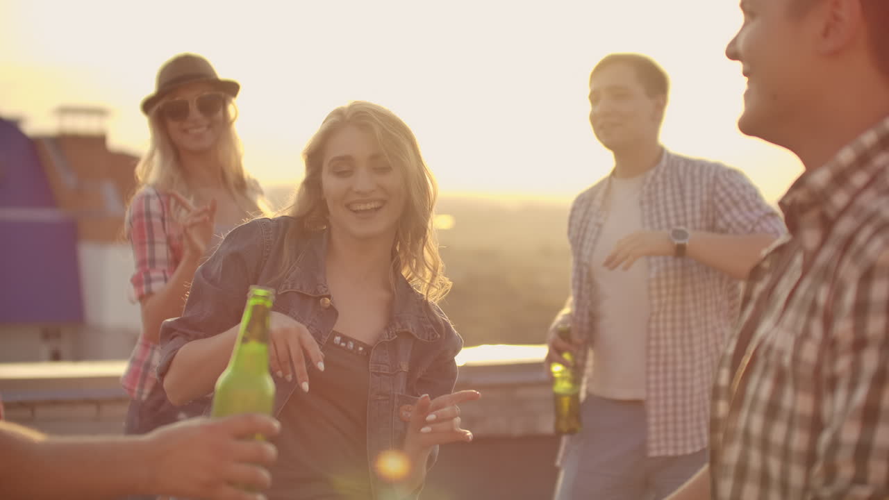 Ragazza che balla a una festa sul tetto, al rallentatore, con un gruppo di amici multirazziali che si divertono; una giovane donna asiatica balla e si gode l'evento sul tetto al tramonto, bevendo alcolici e festeggiando nel fine settimana.