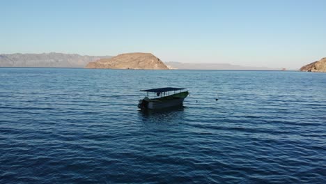 Video-shows-drone-life-flying-away-from-Playa-El-Coyote,-with-a-boat-waiting-on-the-beach,-BCS,-Mexico