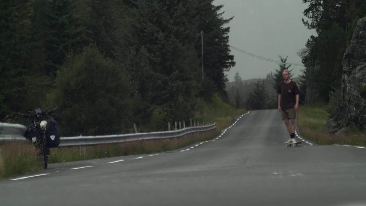 배경의 악천후가 오기 전에 아무데도 없는 길에서 마지막 묘기를 부리는 지친 젊은 스케이트보더