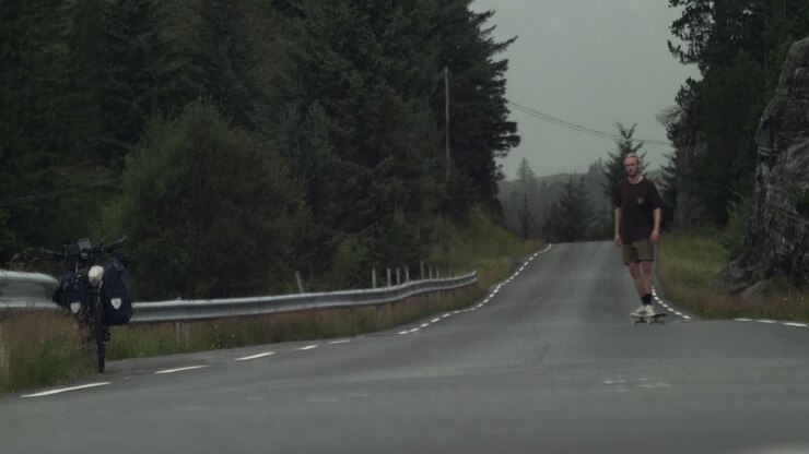 Giovane skateboarder stanco che esegue un ultimo trick, su una strada in mezzo al nulla, prima che arrivi il maltempo sullo sfondo.