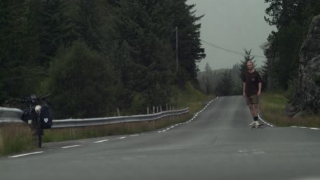 joven patinador cansado haciendo un último truco, en una carretera en medio de la nada, antes de que llegue el mal tiempo en el fondo