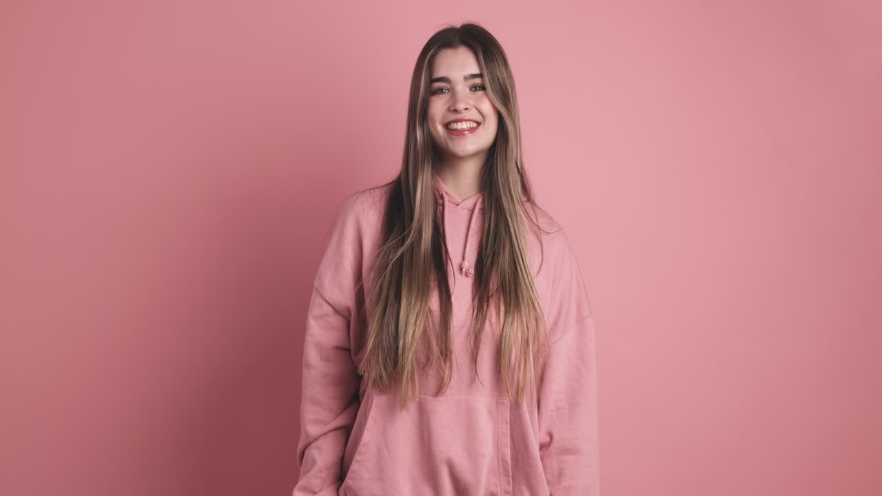 Positing woman with long hair smiling in pink studio