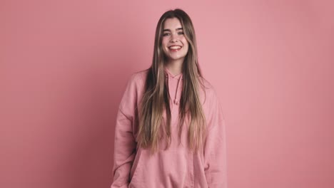 positing woman with long hair smiling in pink studio