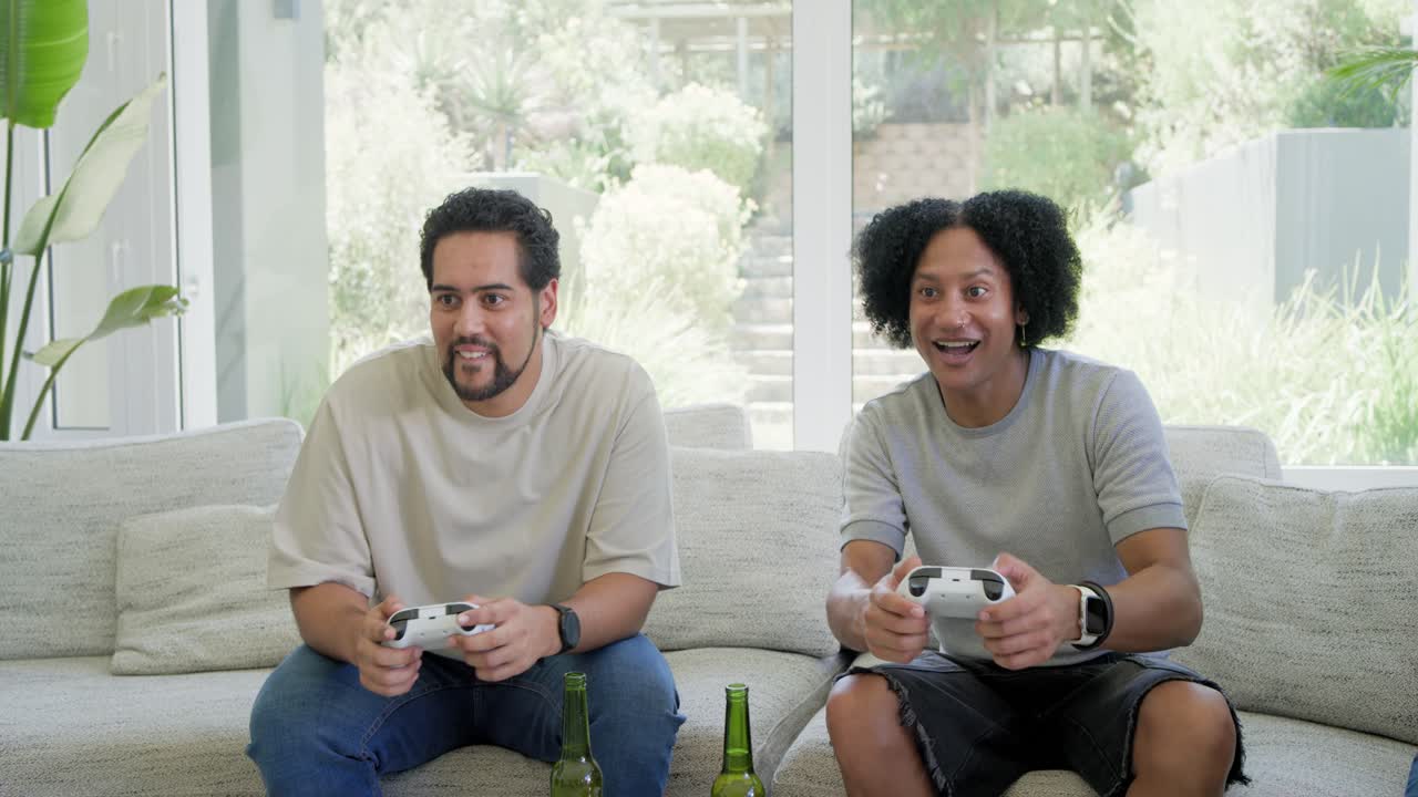 Friends on light couch watching two men gripping white controllers and reacting to decisive play