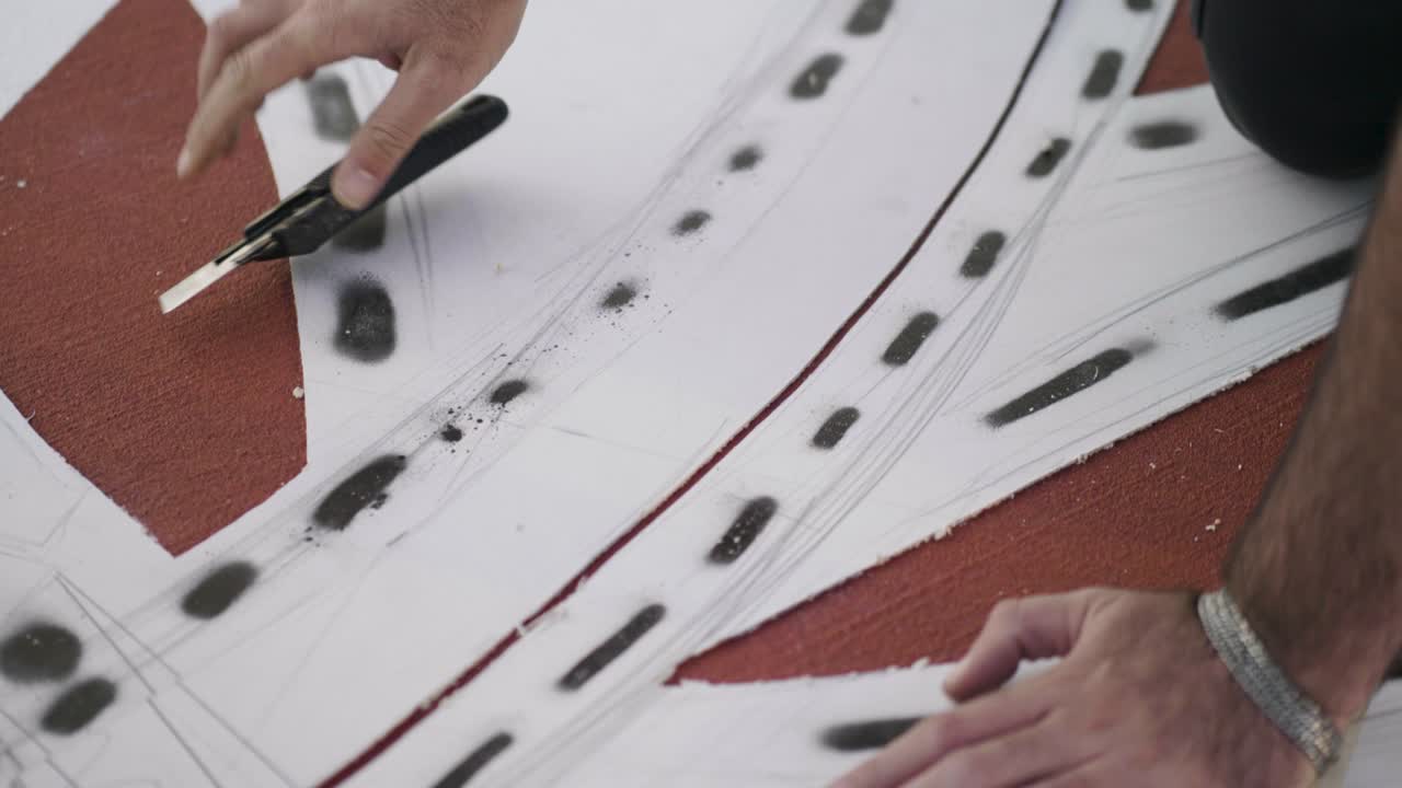 Close-up of an unrecognizable artist's hands cutting paper with a cutter to create a stencil template for geometric art at Neot Smadar Kibbutz, real time.