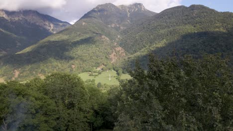 A-breathtaking-drone-ascends-from-a-dense-forest,-unveiling-the-immense-beauty-of-the-Pyrenees-mountain-range