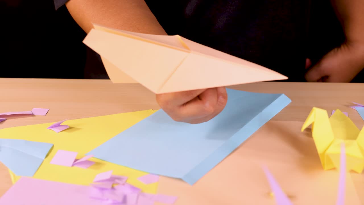 Person folds and presents an origami paper airplane on a colorful, well-lit craft table