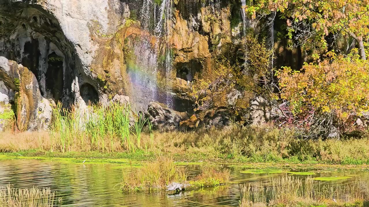 Cascate illuminate dal sole scendono lungo una parete rocciosa coperta di muschio in acque color smeraldo presso il Parco nazionale dei laghi di Plitvice, in Croazia, creando un paesaggio sereno e suggestivo per viaggi naturalistici