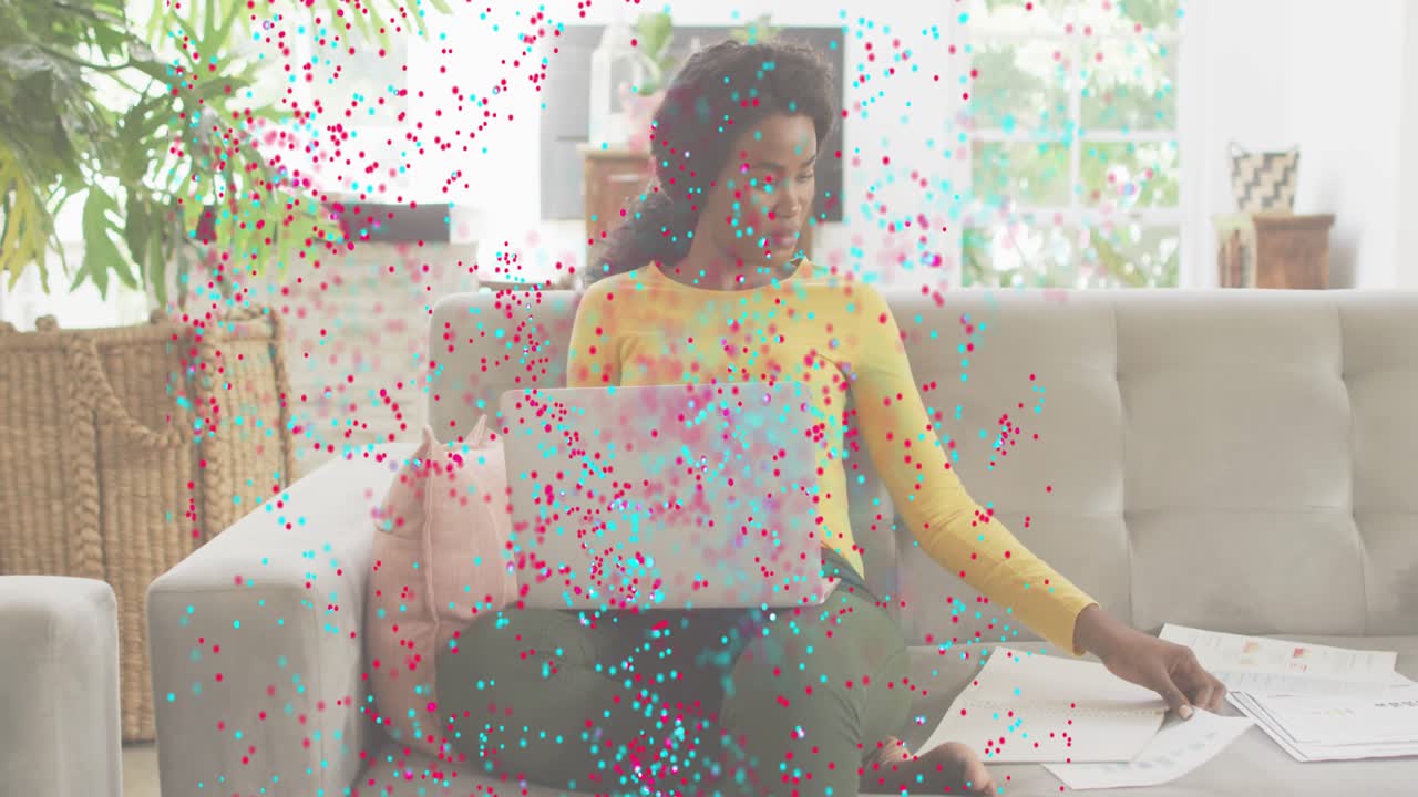 Woman scrolling laptop in home tech demo, spawning pink turquoise particles swirling over papers