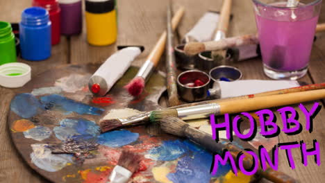 animation of hobby month text in pink, over oil paints, paintbrushes and palette on table