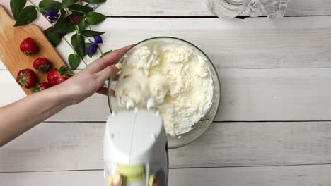 top down shot of whipping heavy cream with mascarpone cheese in glass bowl using hand mixer