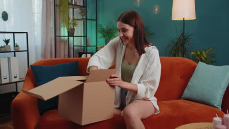 Happy-young-woman-shopper-unpacking-cardboard-box-delivery-parcel-online-shopping-purchase-at-home