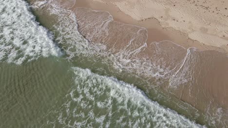 aerial pan drone shot of clear ocean waves slowly breaking on white sand beach