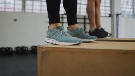 Mid-section-of-fit-caucasian-woman-and-man-jumping-on-pylo-boxes-at-the-gym