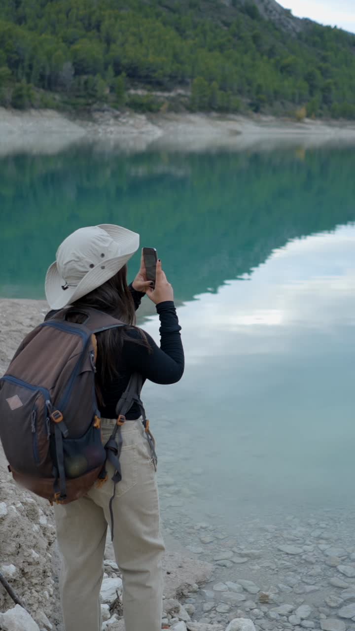 A woman taking a photo of a scenic lake and mountains