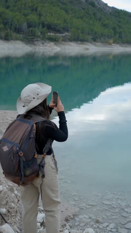 a woman taking a photo of a scenic lake and mountains