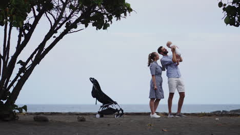 A-Lo-Largo-De-Un-Embarcadero-De-Madera-Bañado-Por-El-Sol,-Una-Feliz-Familia-Caucásica-Camina-Con-Su-Hijo-De-Un-Año-En-Un-Cochecito