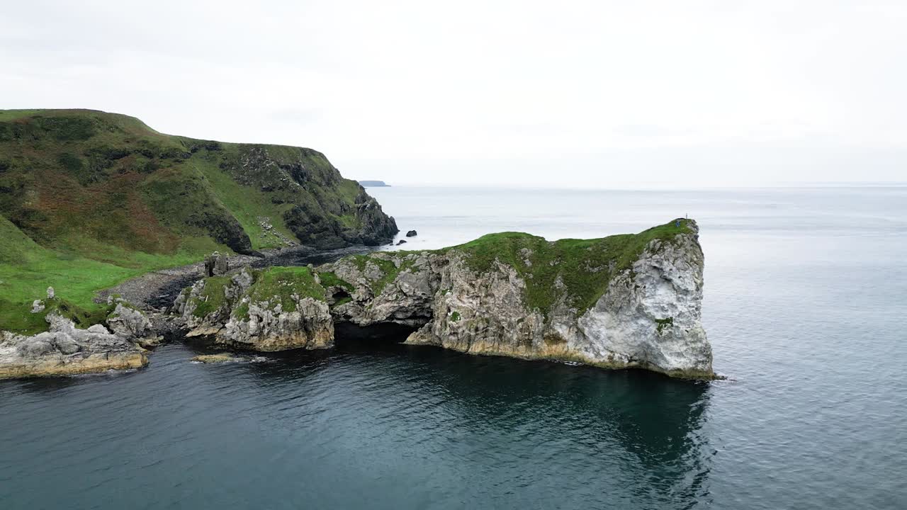 toma aérea de lento ascenso de la hermosa costa con vistas a las rocas en el agua y el tranquilo mar azul desde el castillo de kinbane irlanda del norte a lo largo de la ruta de la carretera gigante durante una mañana nublada