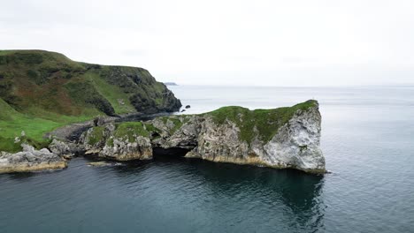 Aerial-slow-ascending-shot-of-the-gorgeous-coastline-overlooking-rocks-in-the-water-and-calm-blue-sea-from-Kinbane-Castle-Northern-Ireland-along-the-Giant-Causeway-Route-during-a-cloudy-morning