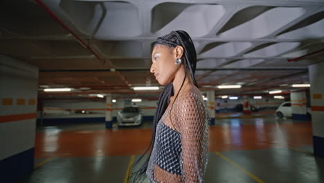 chica de moda de primer plano yendo al estacionamiento nocturno. mujer con dreadlocks mirando la cámara posando